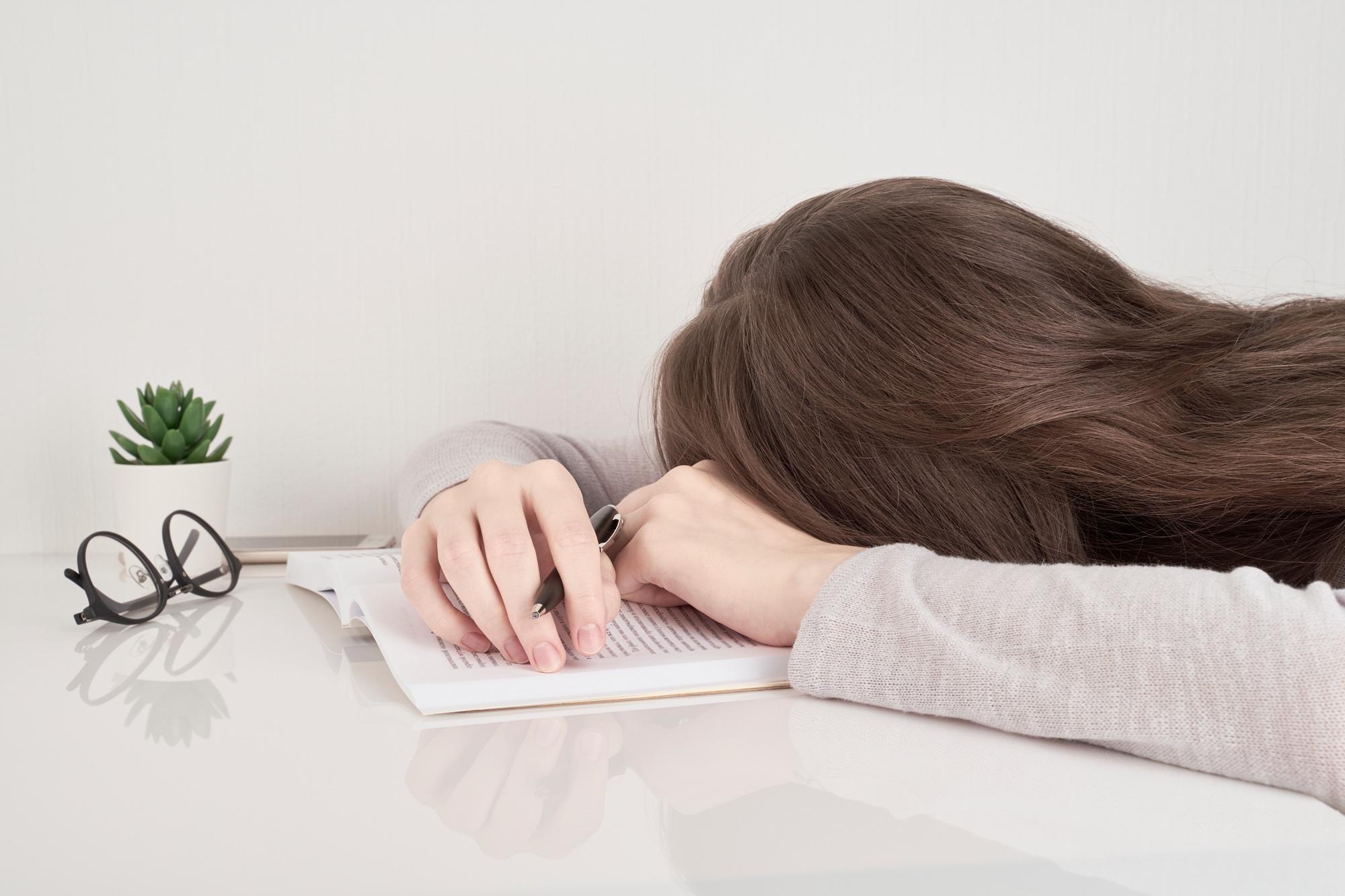 Tired young woman sleeping at table with books, fatigue after school or work